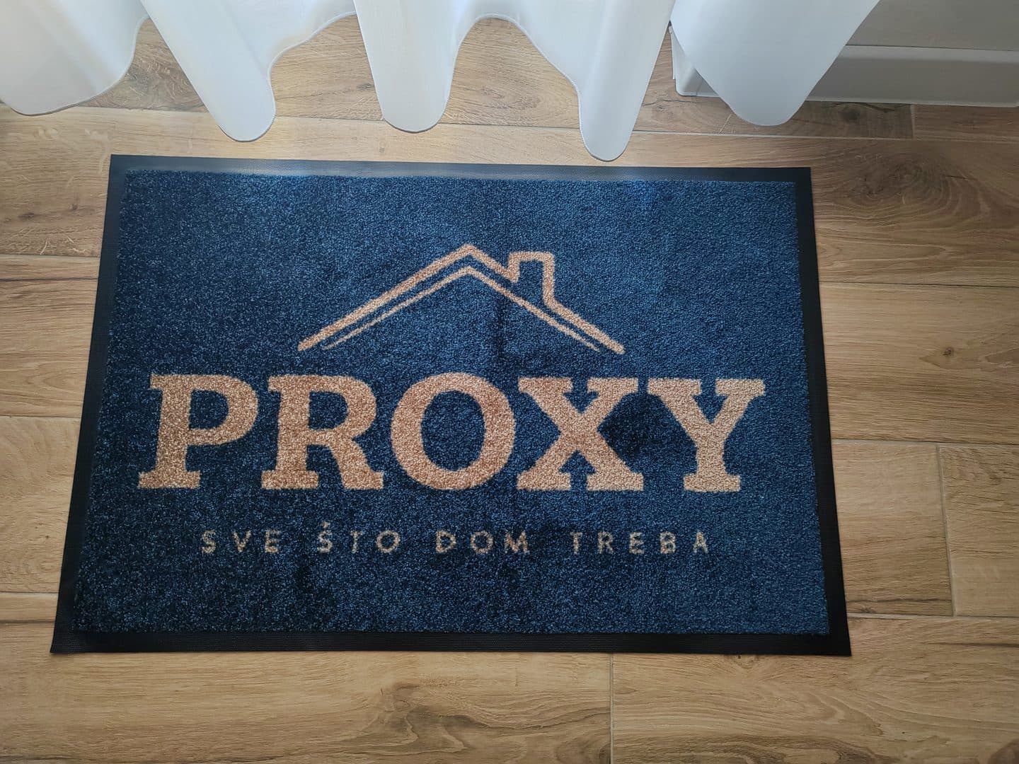 Tamnoplavi otirač Light s logotipom PROXY u boji bakra na drvenom podu
