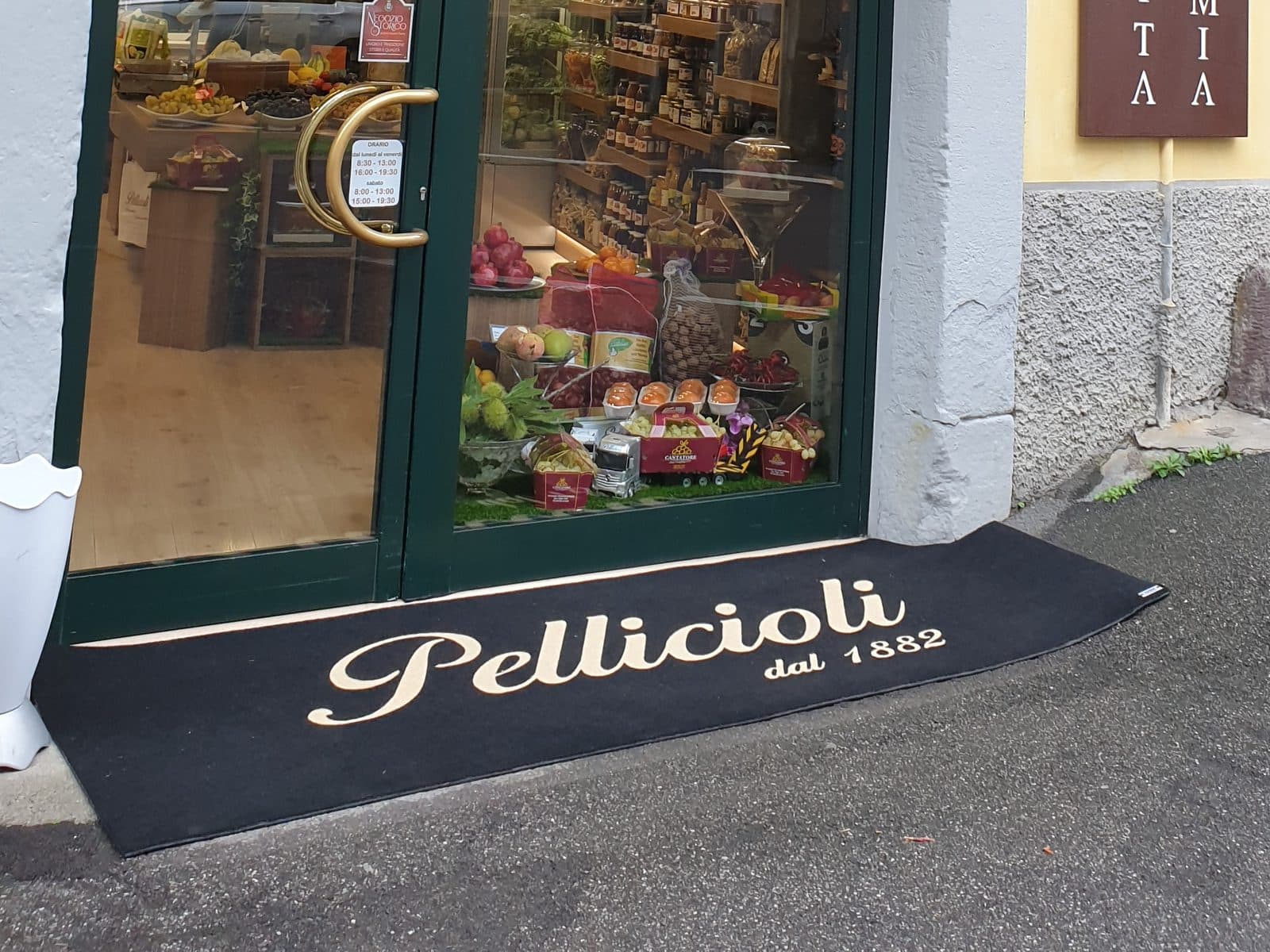 Crni otirač Velluto s bijelim natpisom pred ulazom u trgovinu